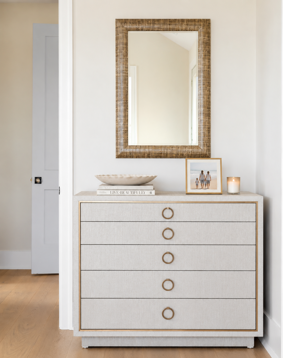 White dresser with circular handles, a large mirror with a woven frame above it, on a light-colored wooden floor.