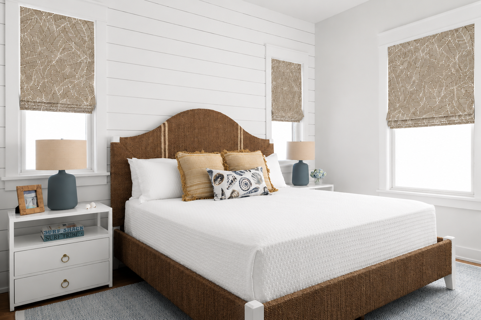 A bedroom with white shiplap walls, two windows, a brown upholstered bed with white bedding, and a small white nightstand on each side. Each nightstand has a gray lamp, a small picture frame, and decorative items. There are decorative pillows on the 