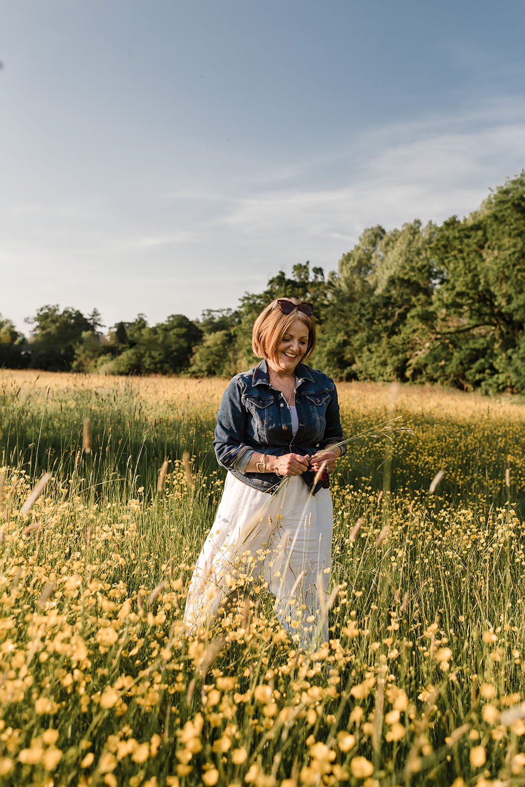 A woman smiling and standing in the middle of a field of yellow buttercups.