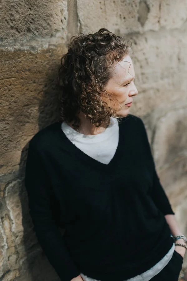 A woman leaning against a stone wall looking away.