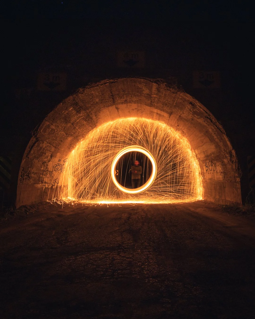 Person performing steel wool spinning inside a tunnel with sparks creating circular light patterns.