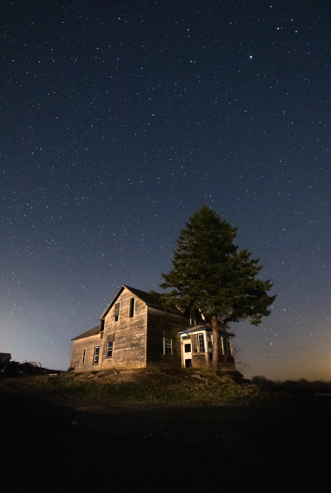 An old wooden house with a large tree next to it, under a star-filled night sky.