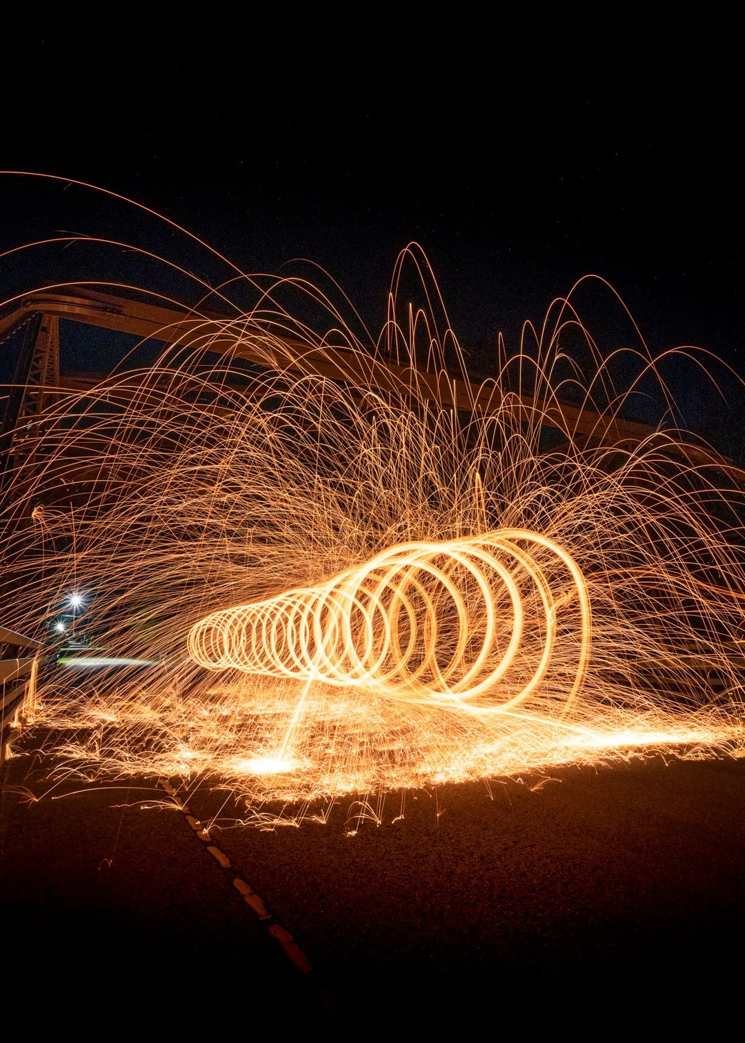 Long exposure of steel wool spinning creating fiery sparks in darkness, with circular light trails and sparks flying outward.