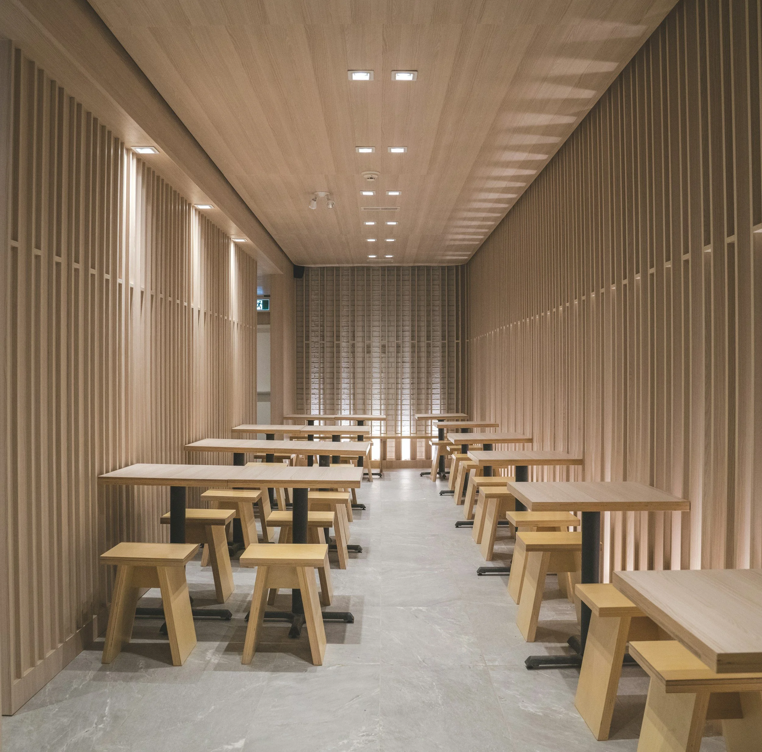 Empty dining area with wooden tables and stools, wood-paneled walls, and ceiling with recessed lighting.