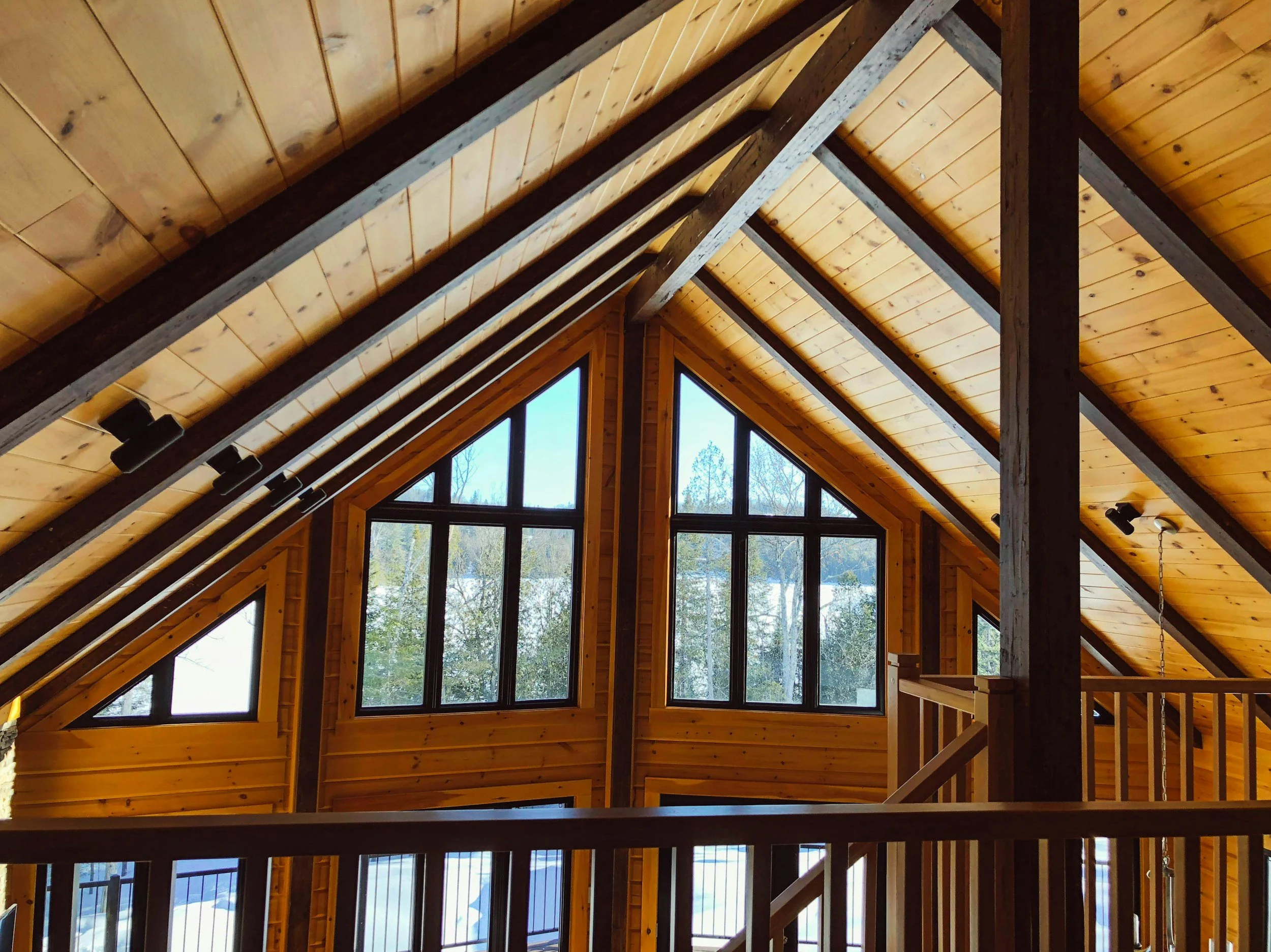 Interior view of a wooden ceiling with large triangular windows letting in natural light, showcasing a mountain landscape outside.