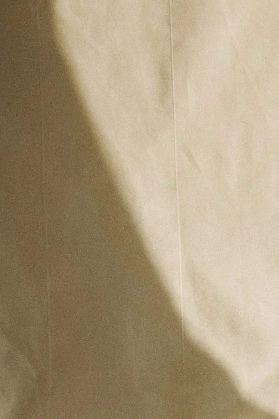 Close-up view of a plain beige wall with a shadow cast across it.