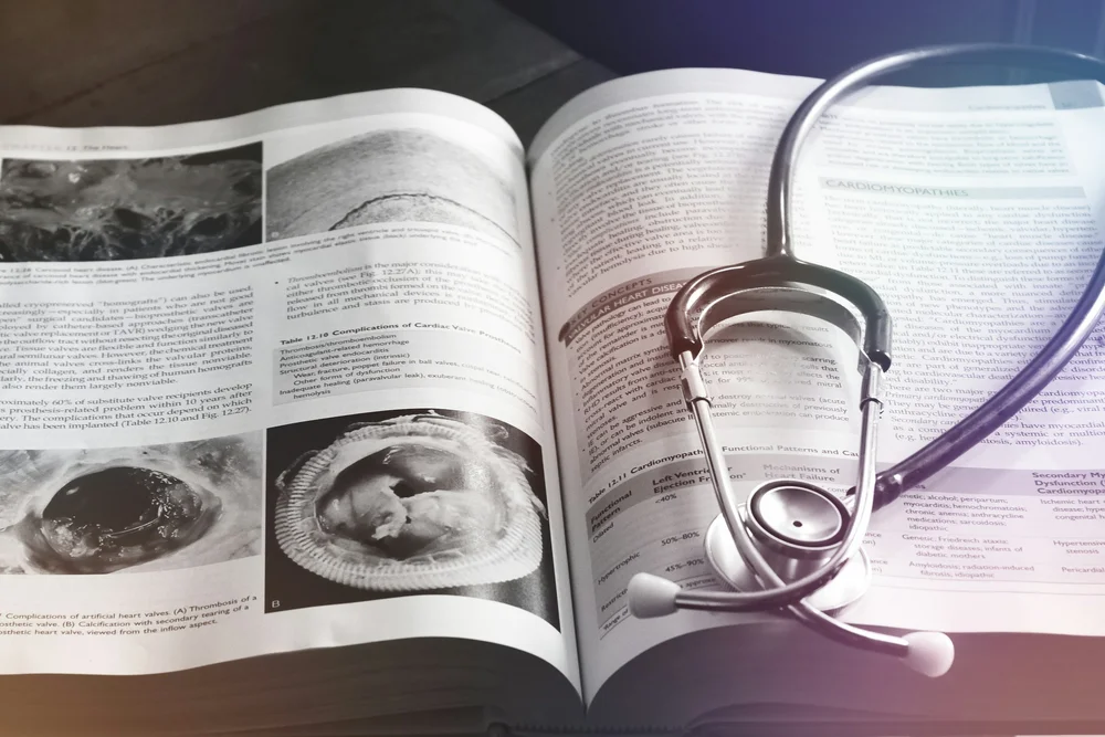 Open book with medical text and images of the heart, accompanied by a stethoscope placed on the pages.
