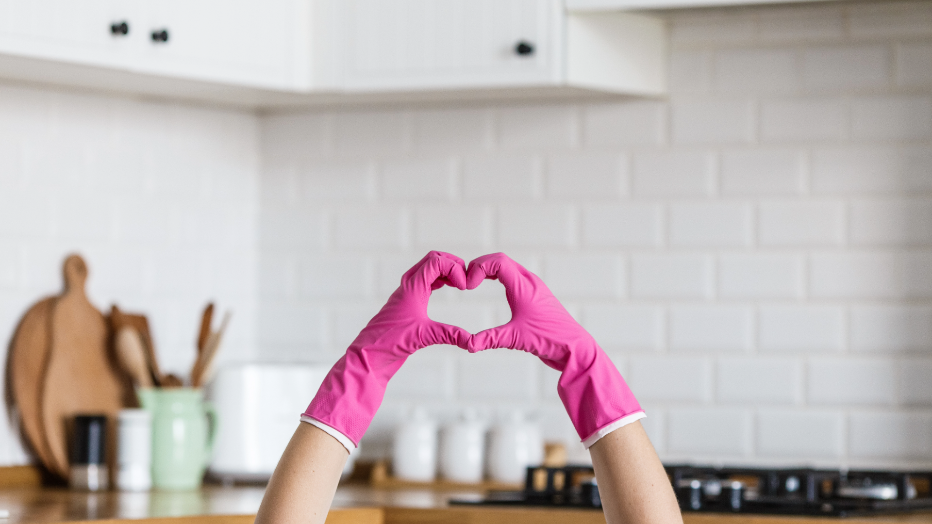 Hands in pink cleaning gloves making a heart shape in front of a clean kitchen