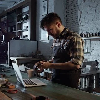A man with a beard and short hair wearing a plaid shirt, working with tools at a workbench in a modern, industrial-style workshop.