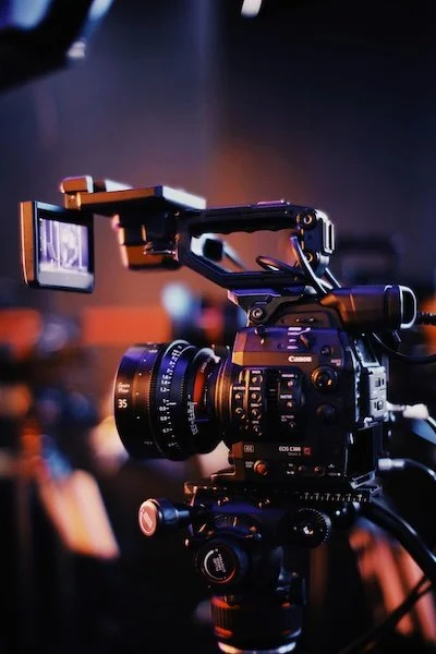 A professional video camera with a mounted monitor on a tripod in a dark studio setting.