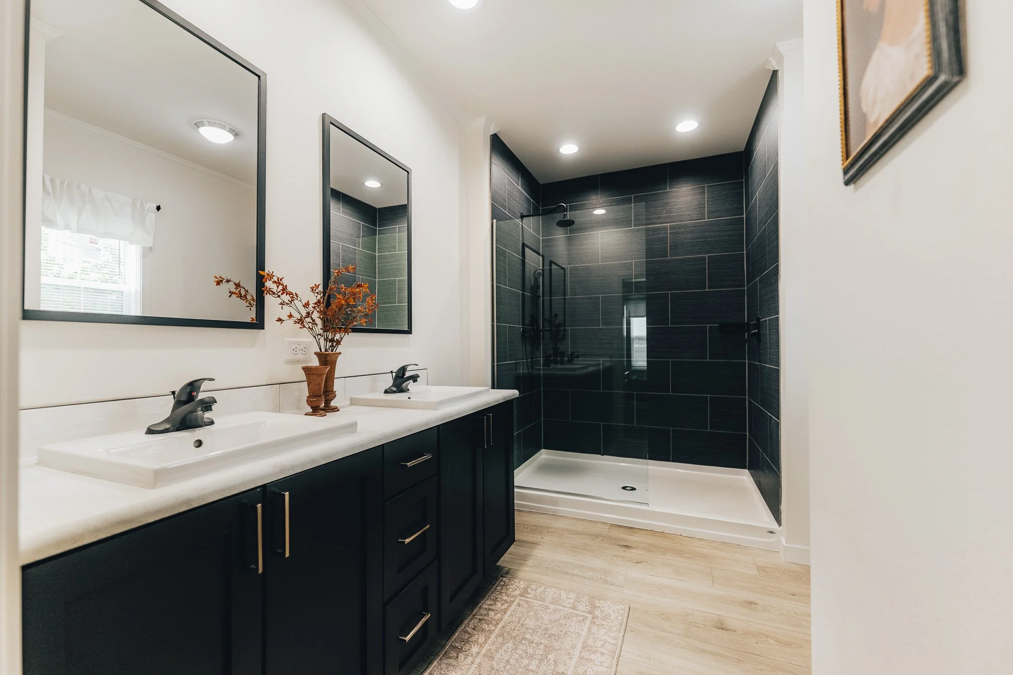 master bathroom with duel vanity and walk in tiled shower with black tiles and rain fall shower head with a half glass wall