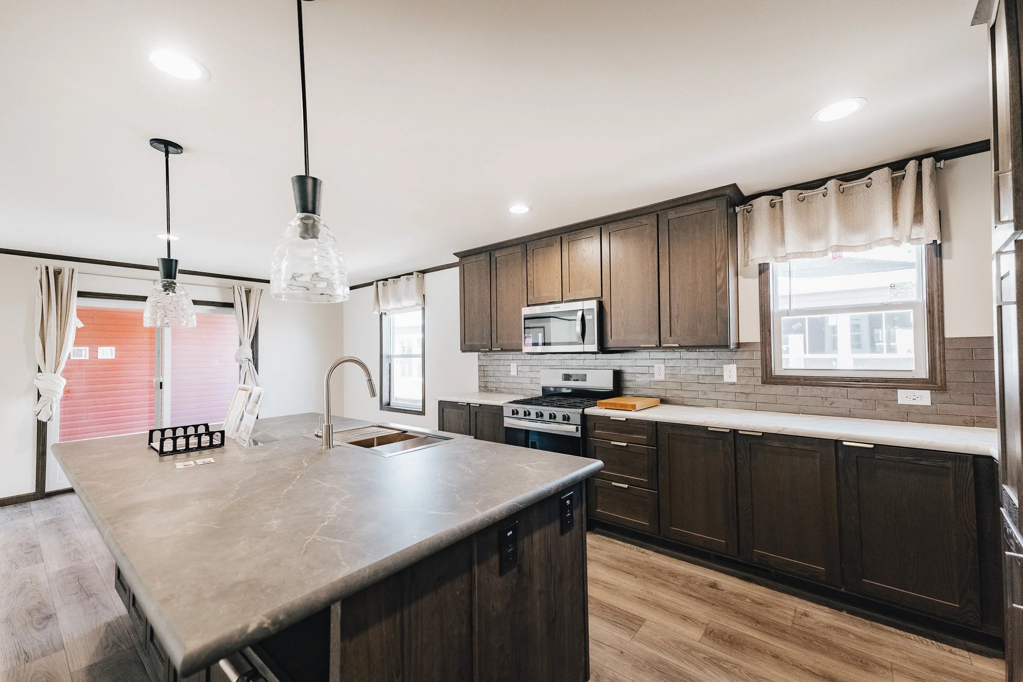 countertop with sink in the island and range with upper cabinets looking into the dinning room area and out into the covered porch. 