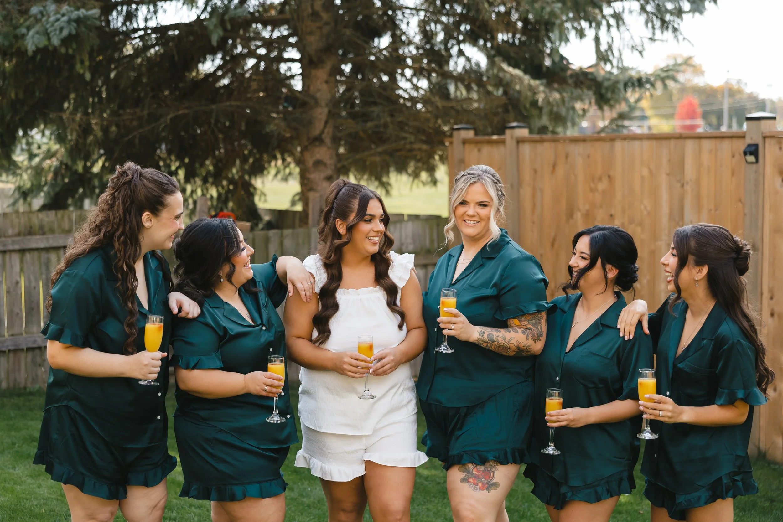 Group of women celebrating outdoors, holding glasses of orange juice, smiling and talking to each other.