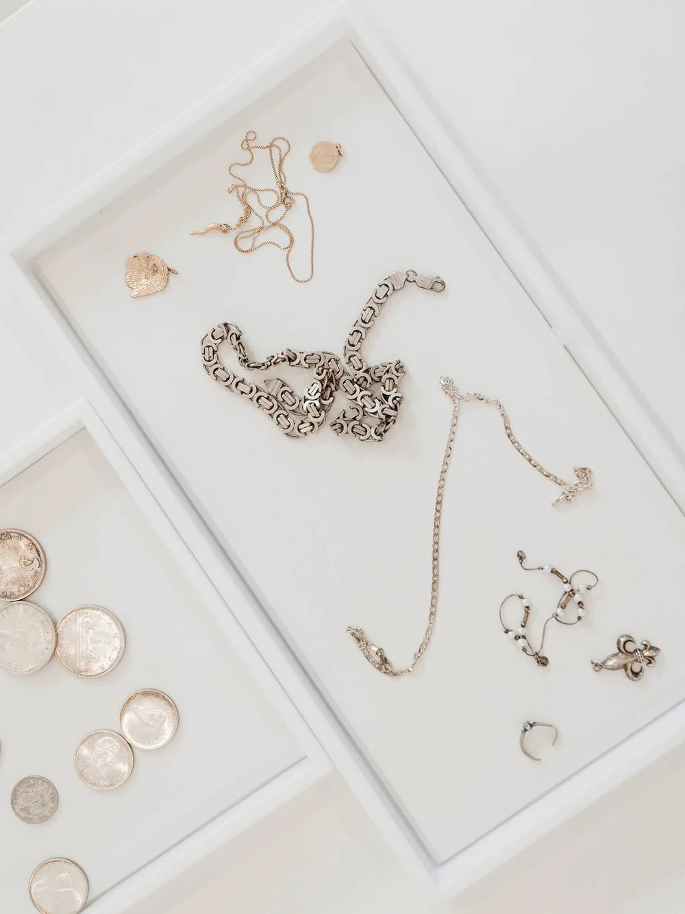 Gold and silver necklaces, bracelets, earrings and rings with scattered coins on a white surface