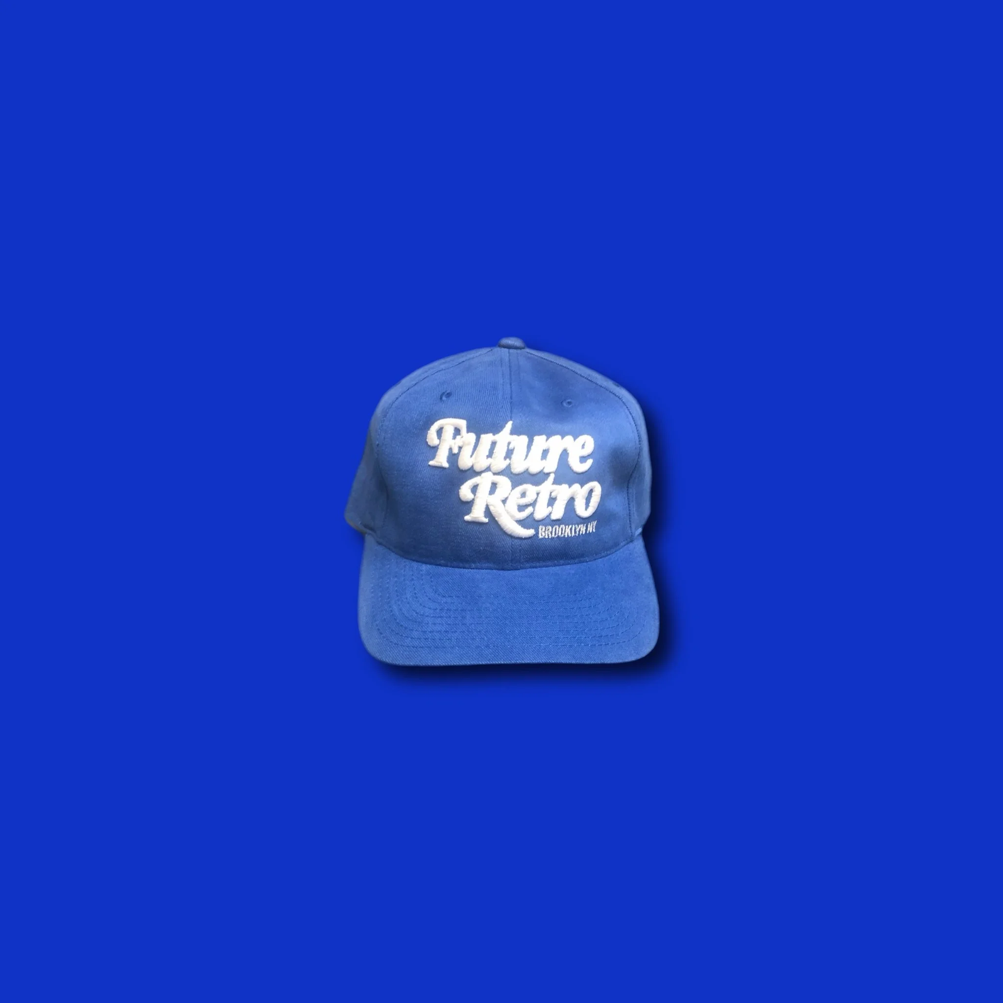 Blue baseball cap with white embroidery that reads "Future Retro Brooklyn NY" against a blue background.
