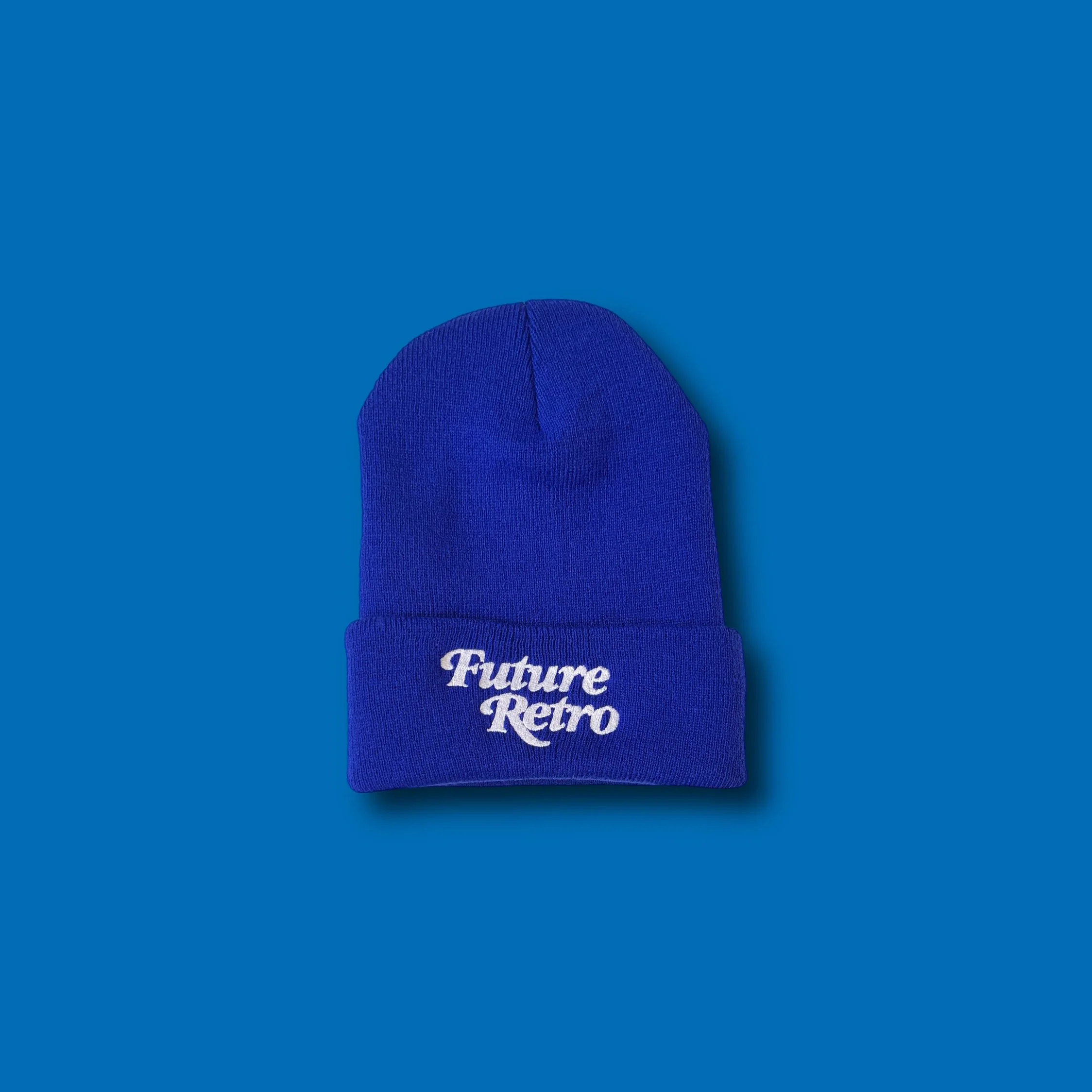 Blue knit beanie hat with white embroidered text that says 'Future Retro' on the front, placed on a blue background.
