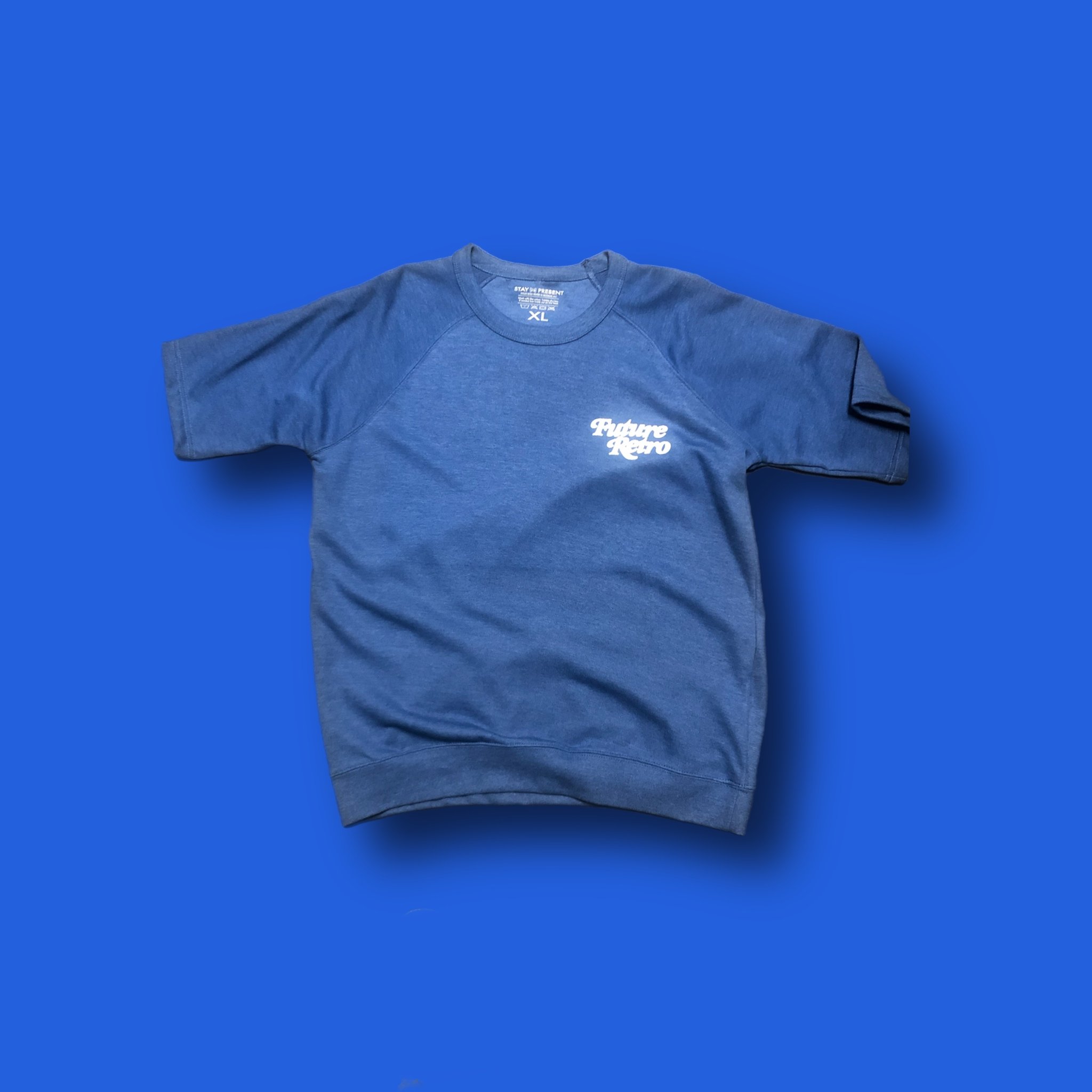 Blue sweatshirt with white text that reads 'Future Retro' on the front, lying on a solid blue background.