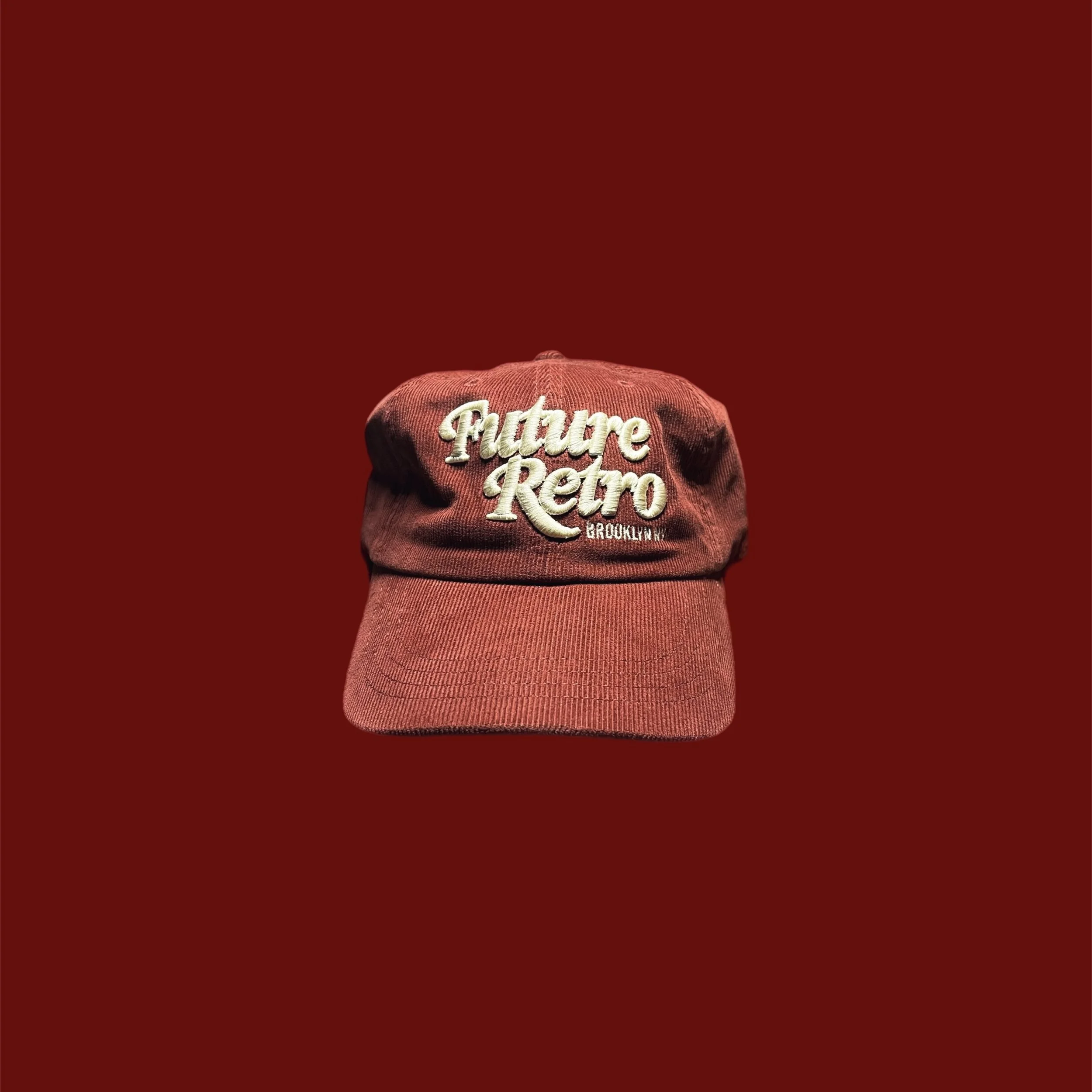Red baseball cap with white embroidered text 'Future Retro Brooklyn' on the front, placed against a red gradient background.