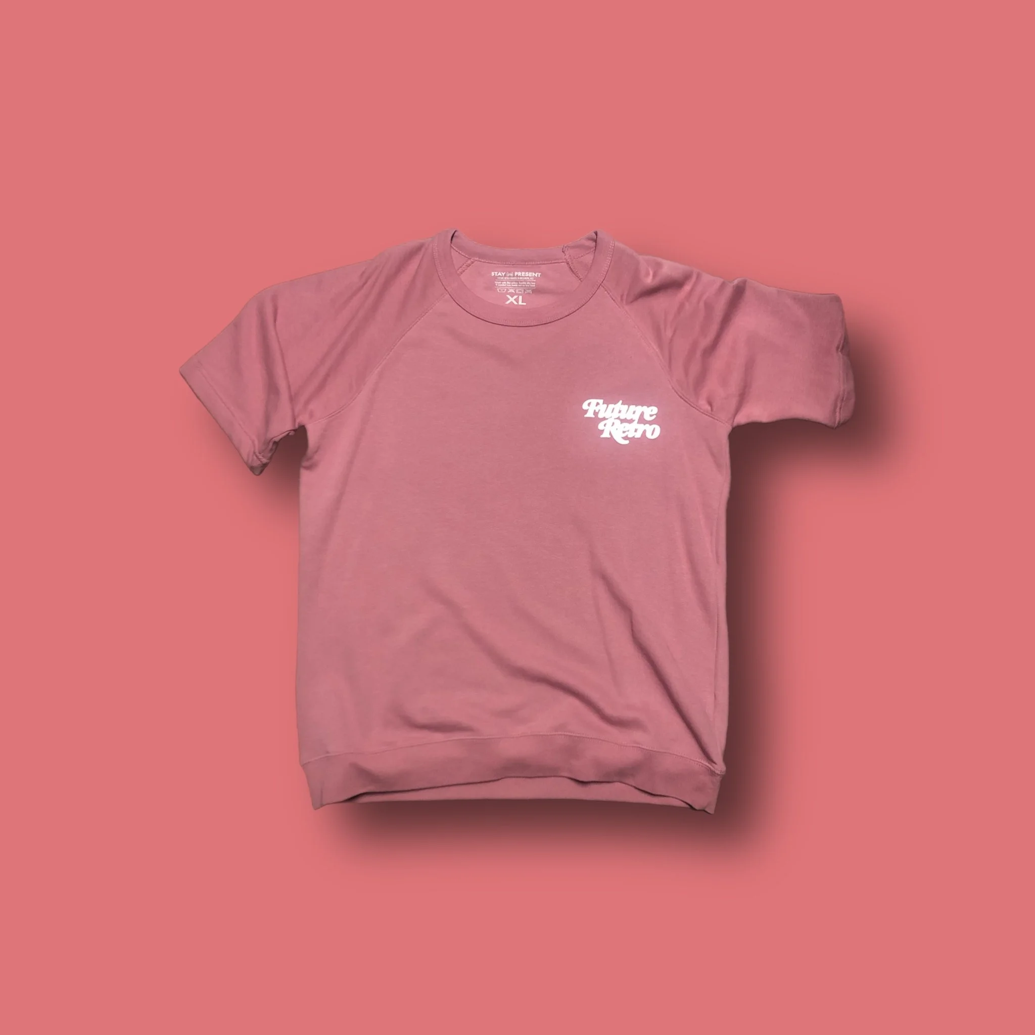 Pink t-shirt with white text logo on the front that says 'Future Retro' lying flat on a matching pink background.
