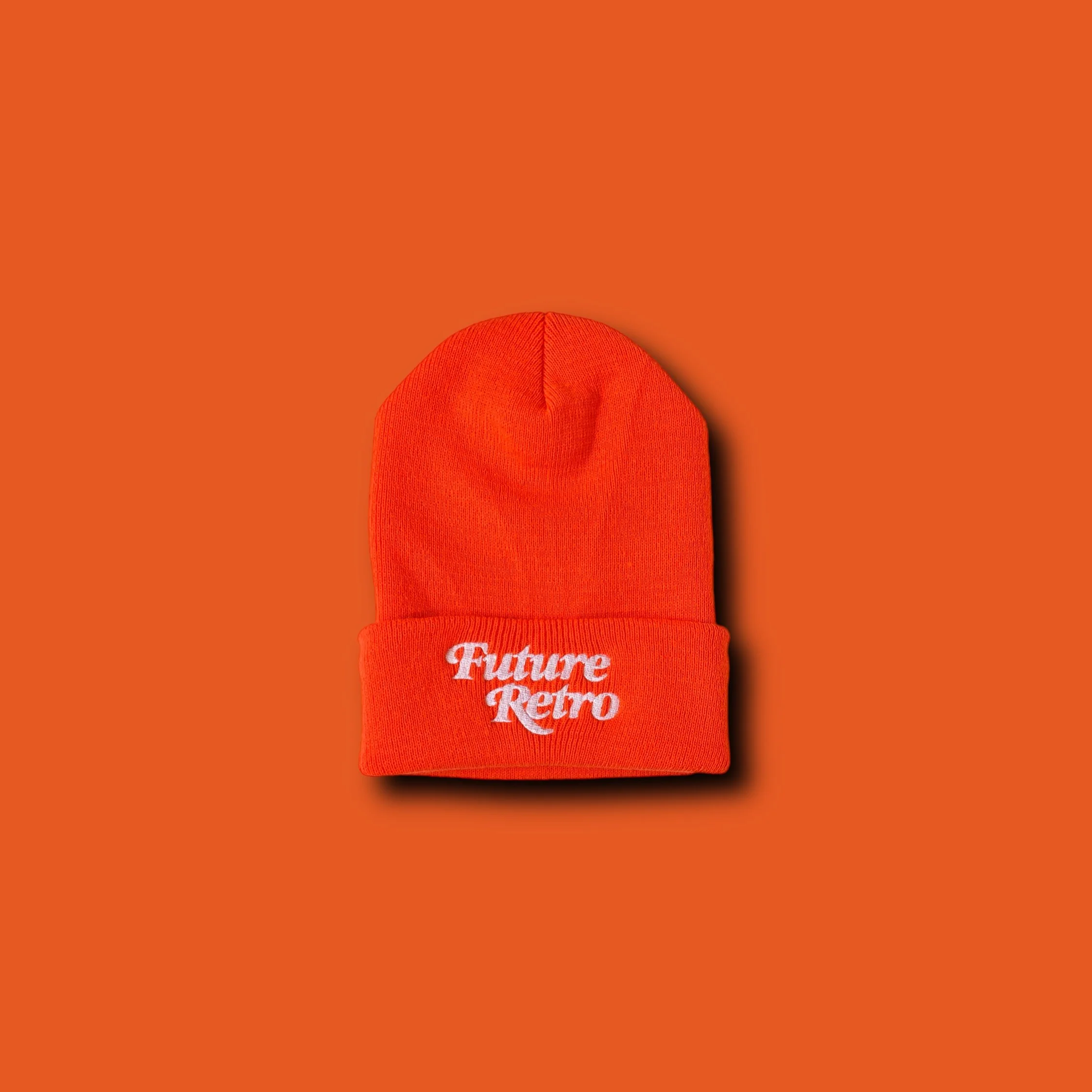 Orange knit beanie hat with white embroidered text 'Future Retro' on the front, placed on an orange background.