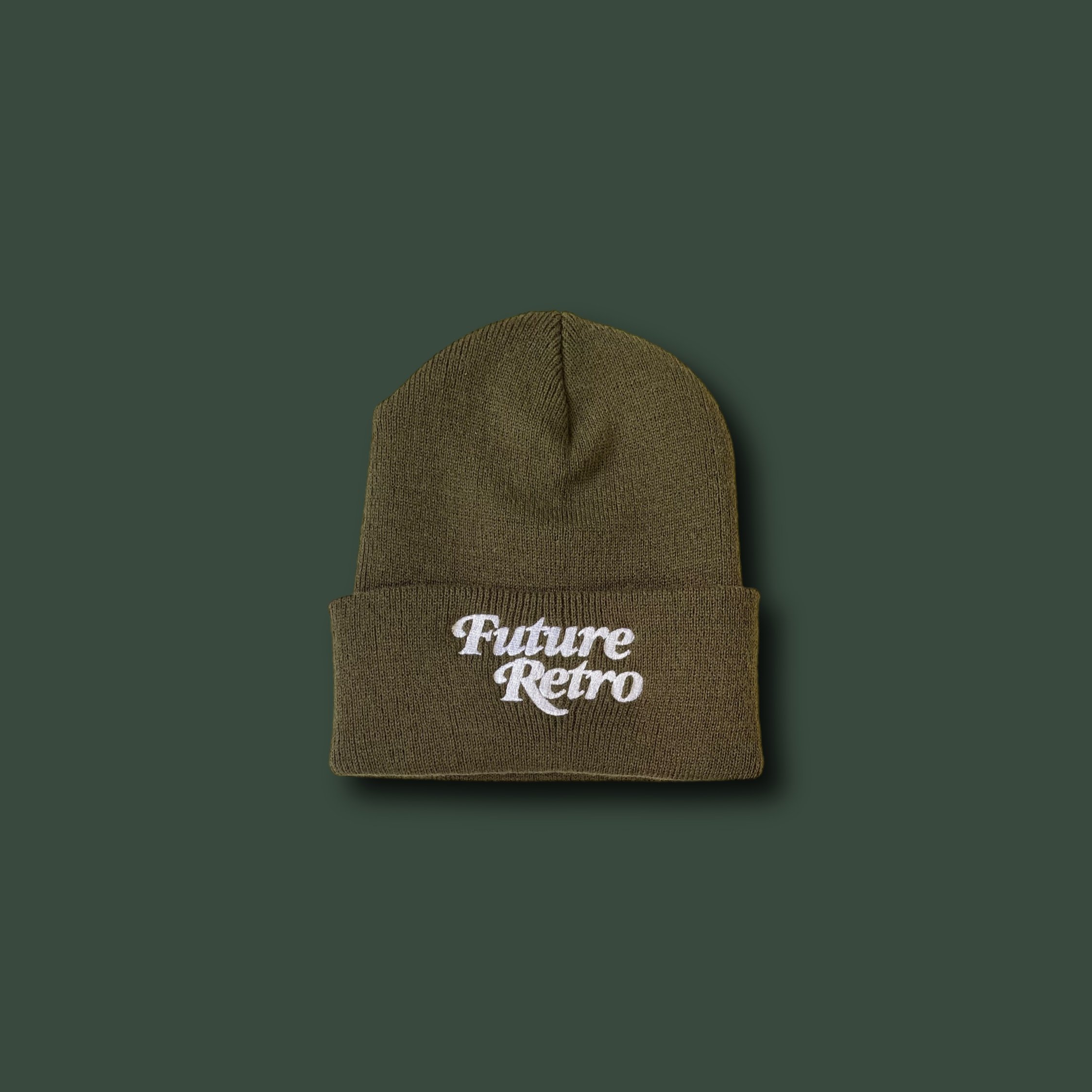 Olive green knit beanie hat with white embroidered text 'Future Retro' on the front, placed on a dark green background.