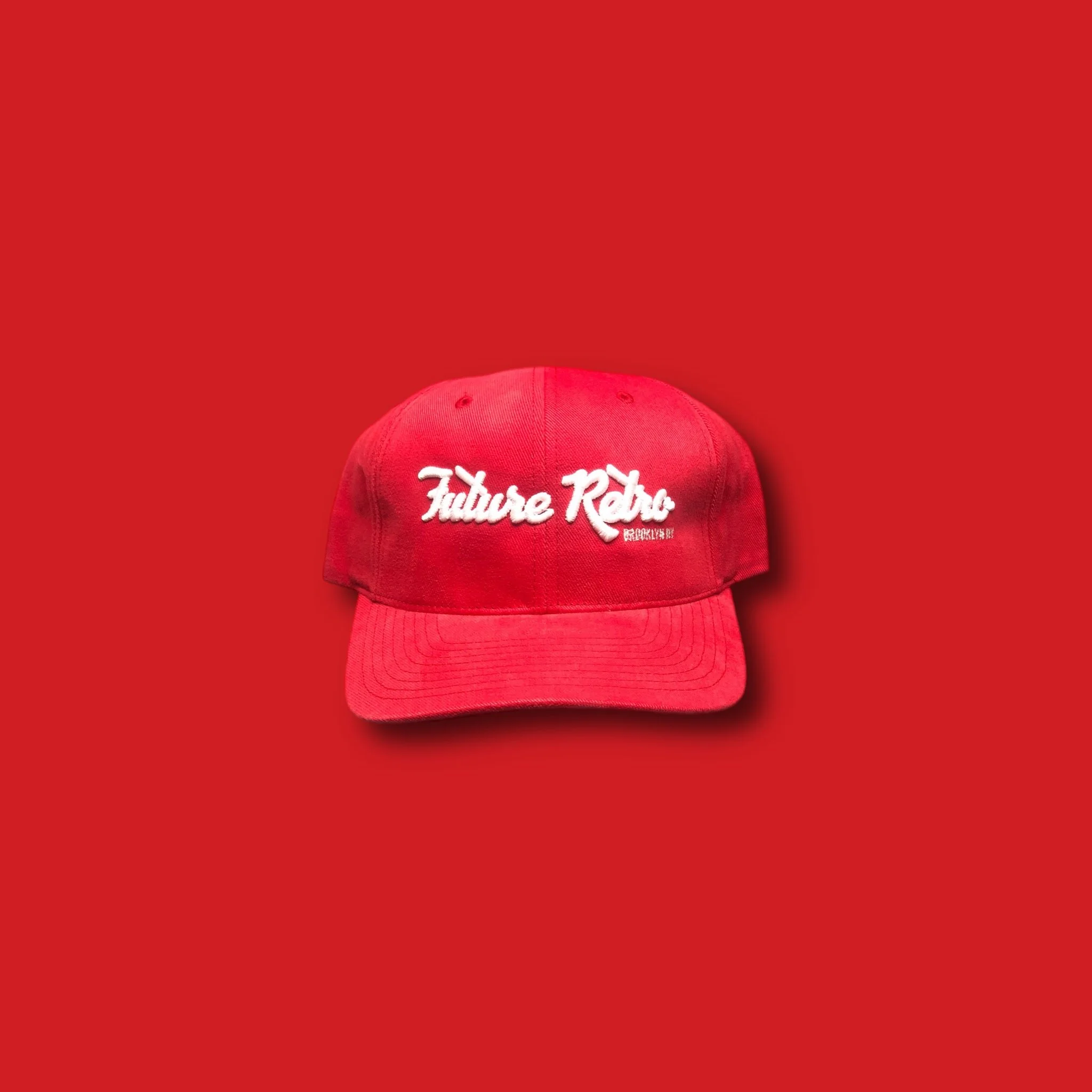Red baseball cap with white embroidered text 'Future Retro' on front, placed on a red background.
