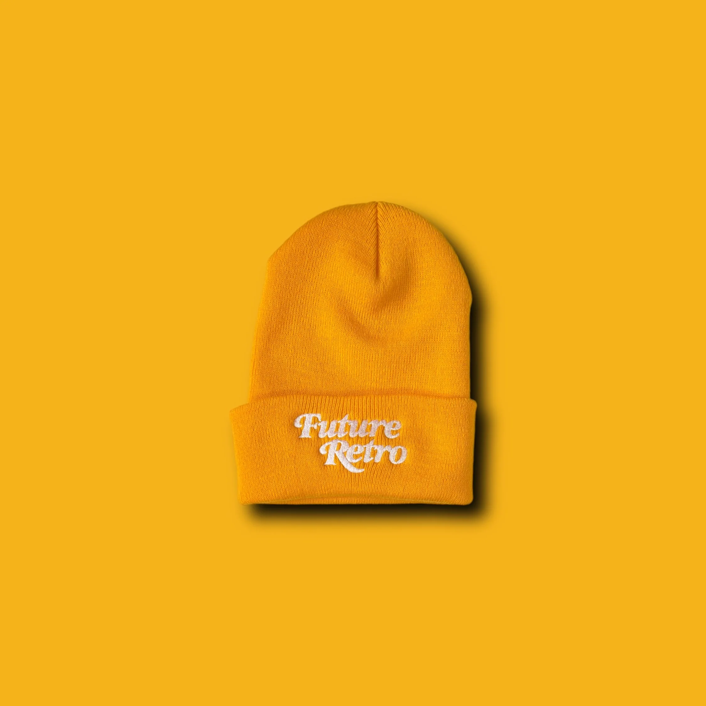 Yellow beanie hat with white embroidered text saying 'Future Retro' on the cuff, placed on a yellow background.