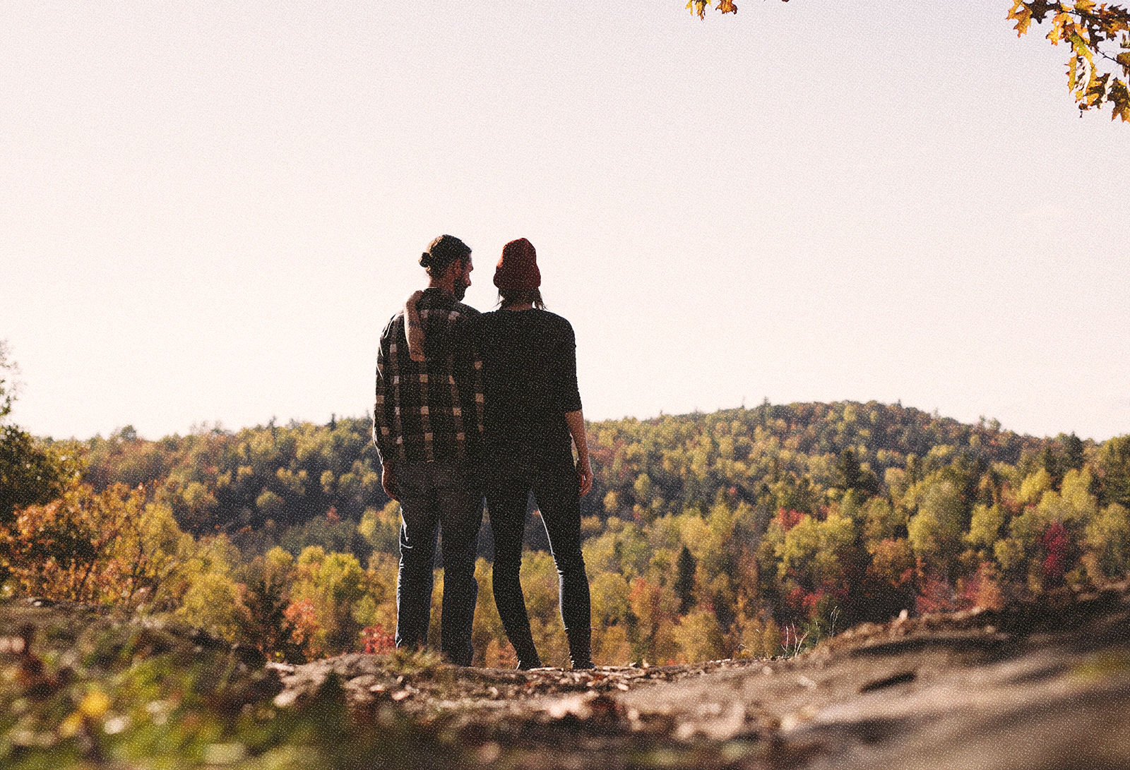 Image of a couple standing together and looking out at a landscape of trees and hills