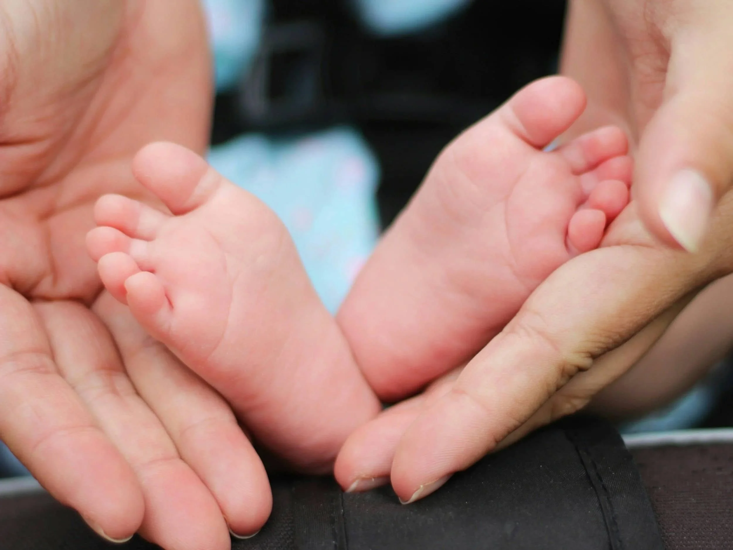 A close-up of an adult person's hand gently holding a baby's feet. Improved parent child relationship after family therapy in Golden Colorado.