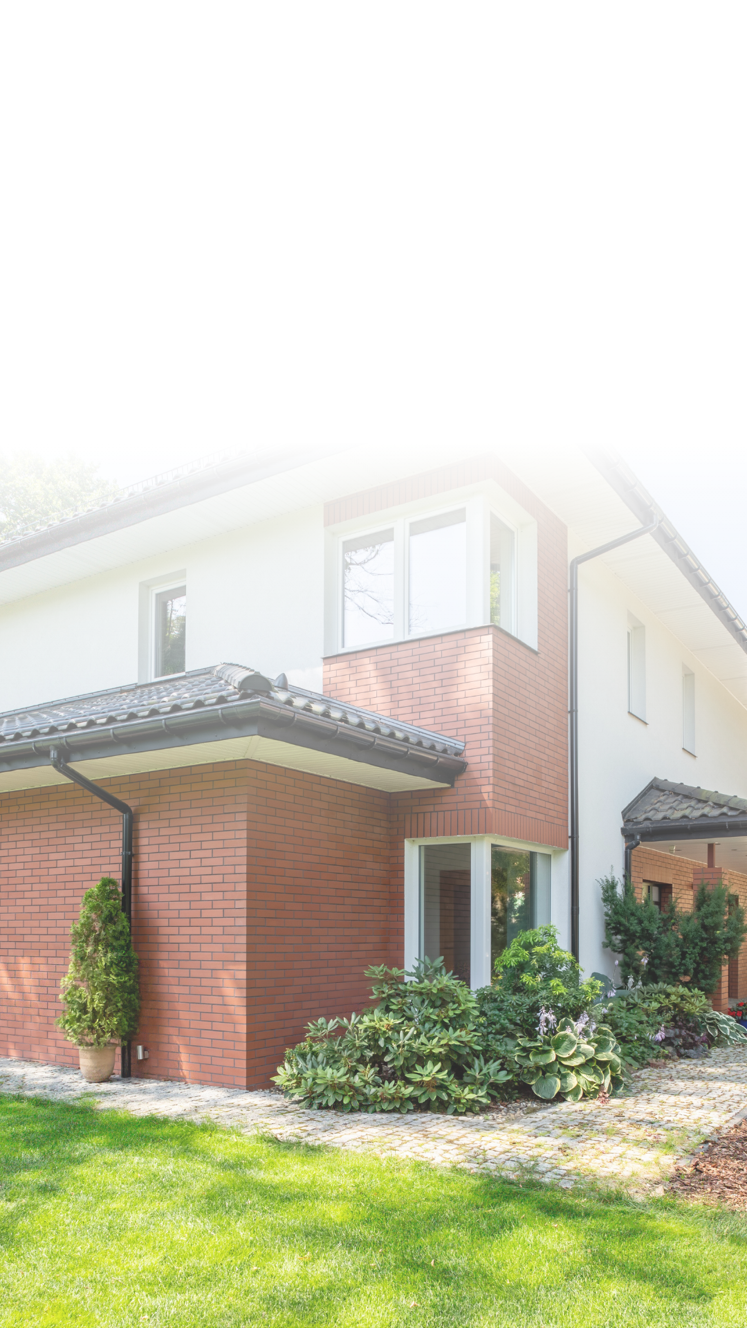 Modern two-story house with brick and white exterior, large windows, landscaped front yard, green lawn, and garden plants.