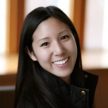 Young woman with long black hair smiling indoors.