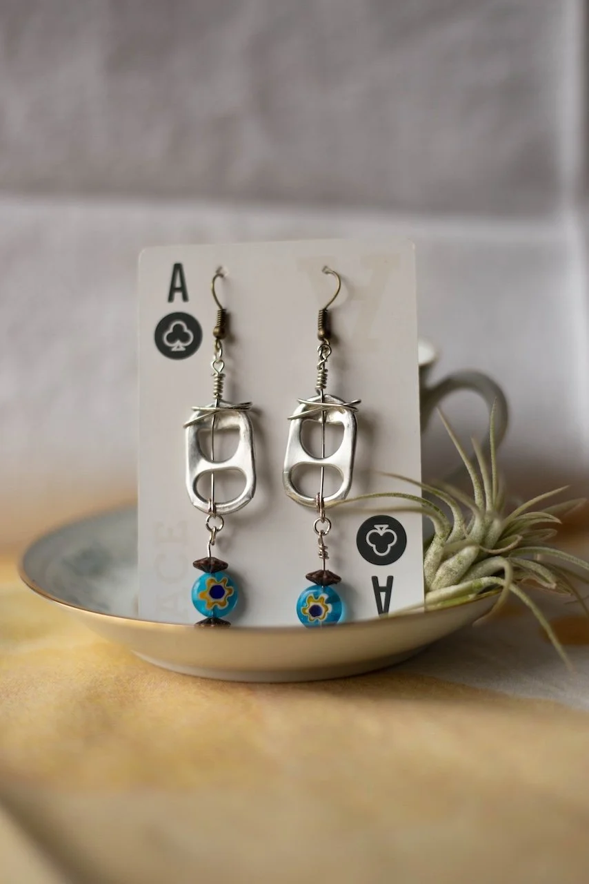 Handmade earrings displayed on playing card with plant in background