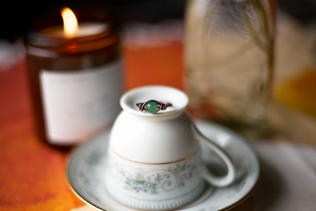 Green stone ring on inverted teacup with candle in background.