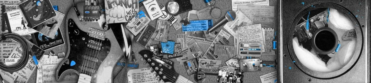 A cluttered workspace with a guitar, musical equipment, papers, and electronic devices scattered across a desk, with a turntable on the right.
