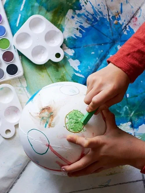 Child painting a ball during a creative art activity.