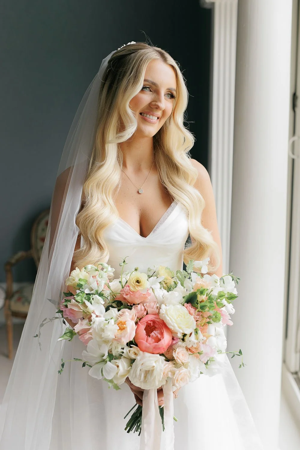 bride holding her bouquet next to window. Portrait of bride with long blonde curly hair