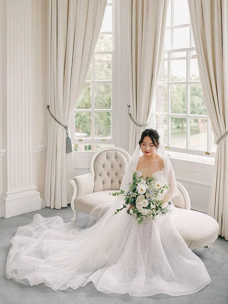 Fine Art Wedding Photography - Bride sitting on a chaise longue by a window in the bridal suite of a manor house in the UK