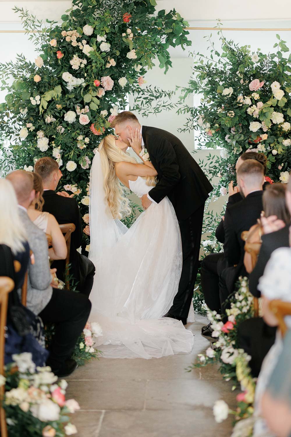 First kiss at wedding, bride and groom in front of big floral arch at Boconnoc