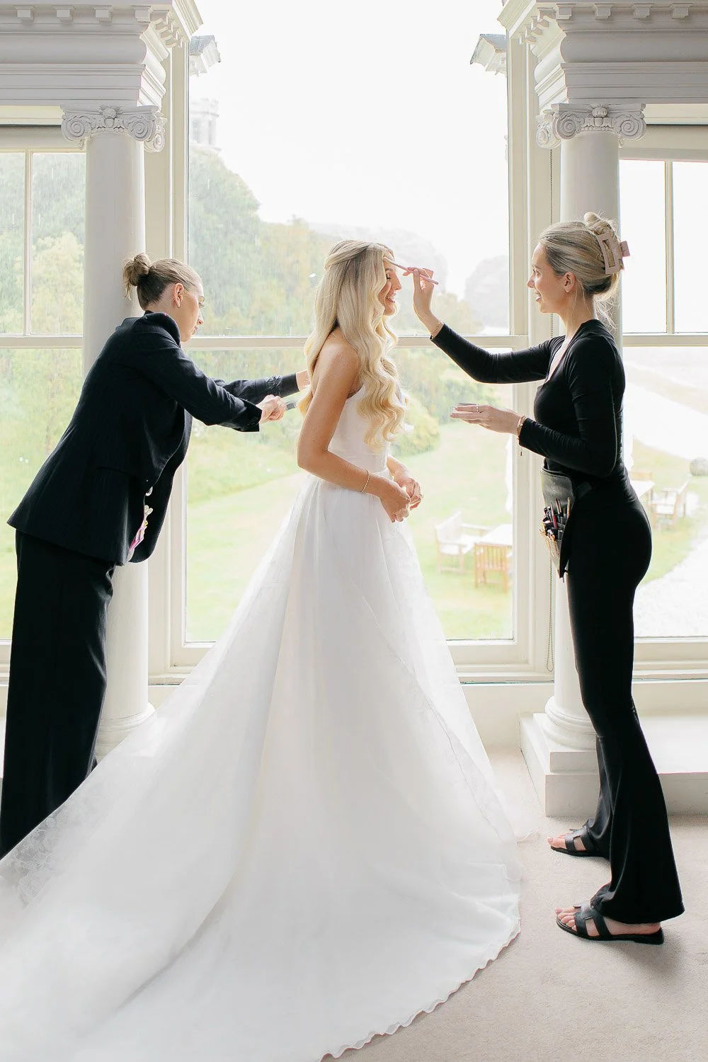 hair and makeup artists finishing touches in front of window at Boconnoc
