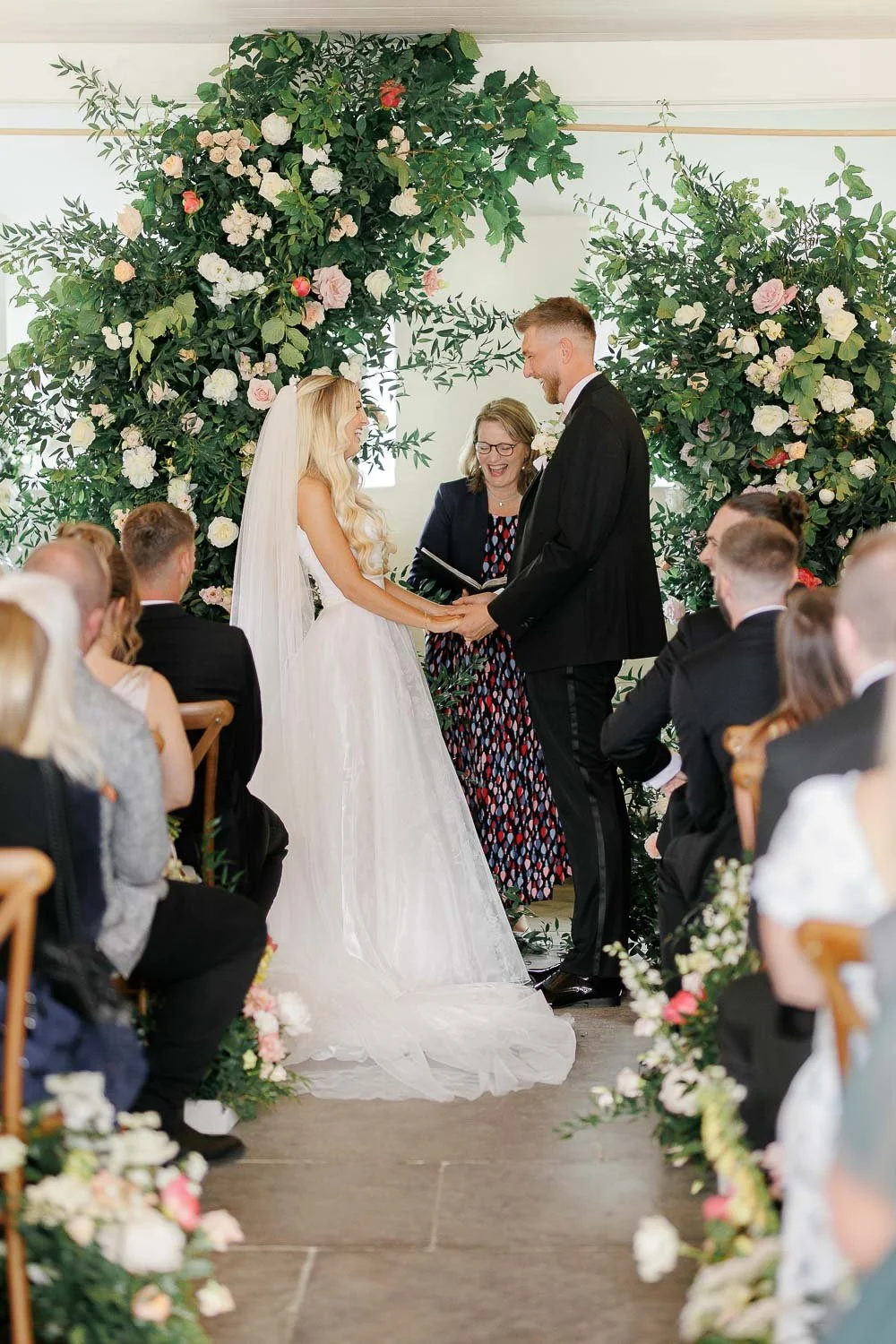 bride and groom in front of big floral arch