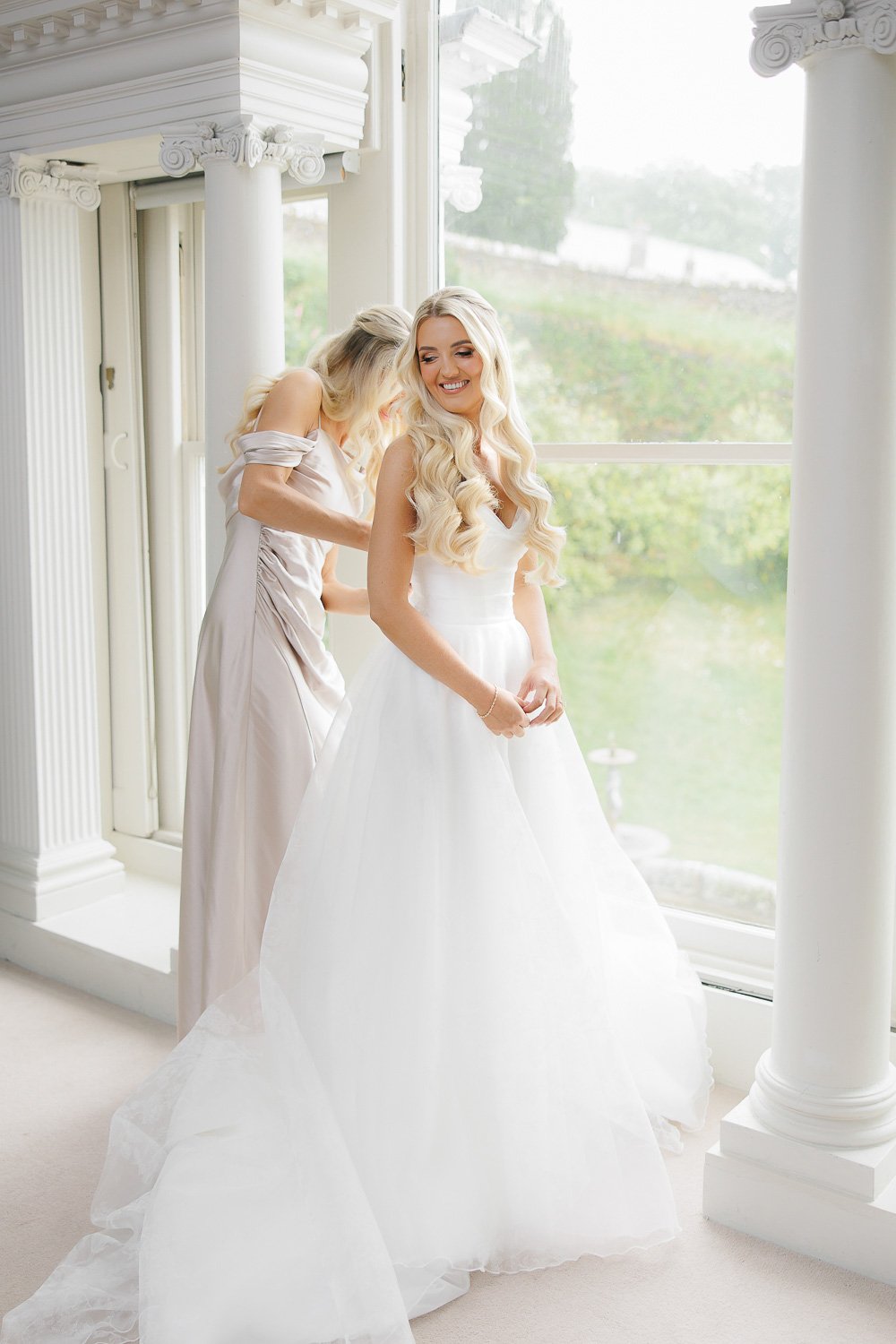 Bride getting into her dress with help of bridesmaid. Interior at Boconnoc