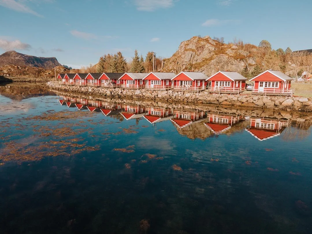 Red wooden houses with white trim, metal roofs, and mountains in the background under a clear blue sky.