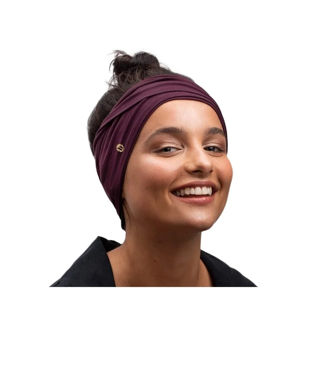 Smiling young woman with brown hair in a bun, wearing a purple headscarf and black jacket, against a white background.