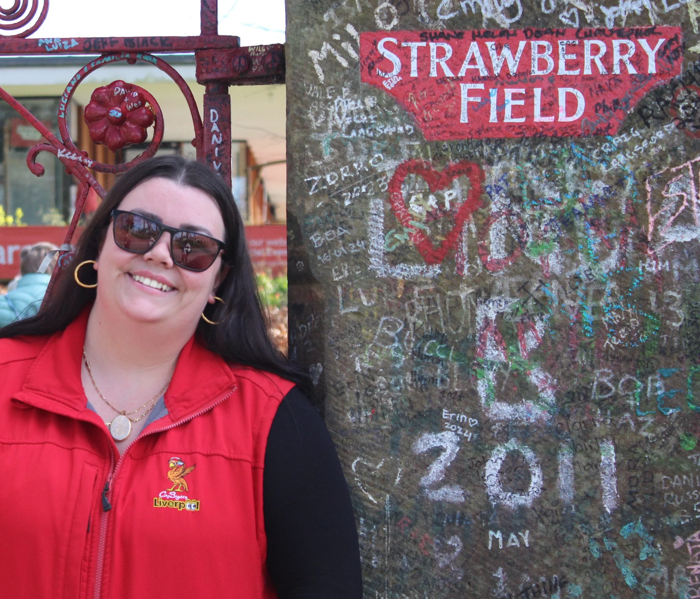 Person in sunglasses standing next to a wall with graffiti and a "Strawberry Field" sign.