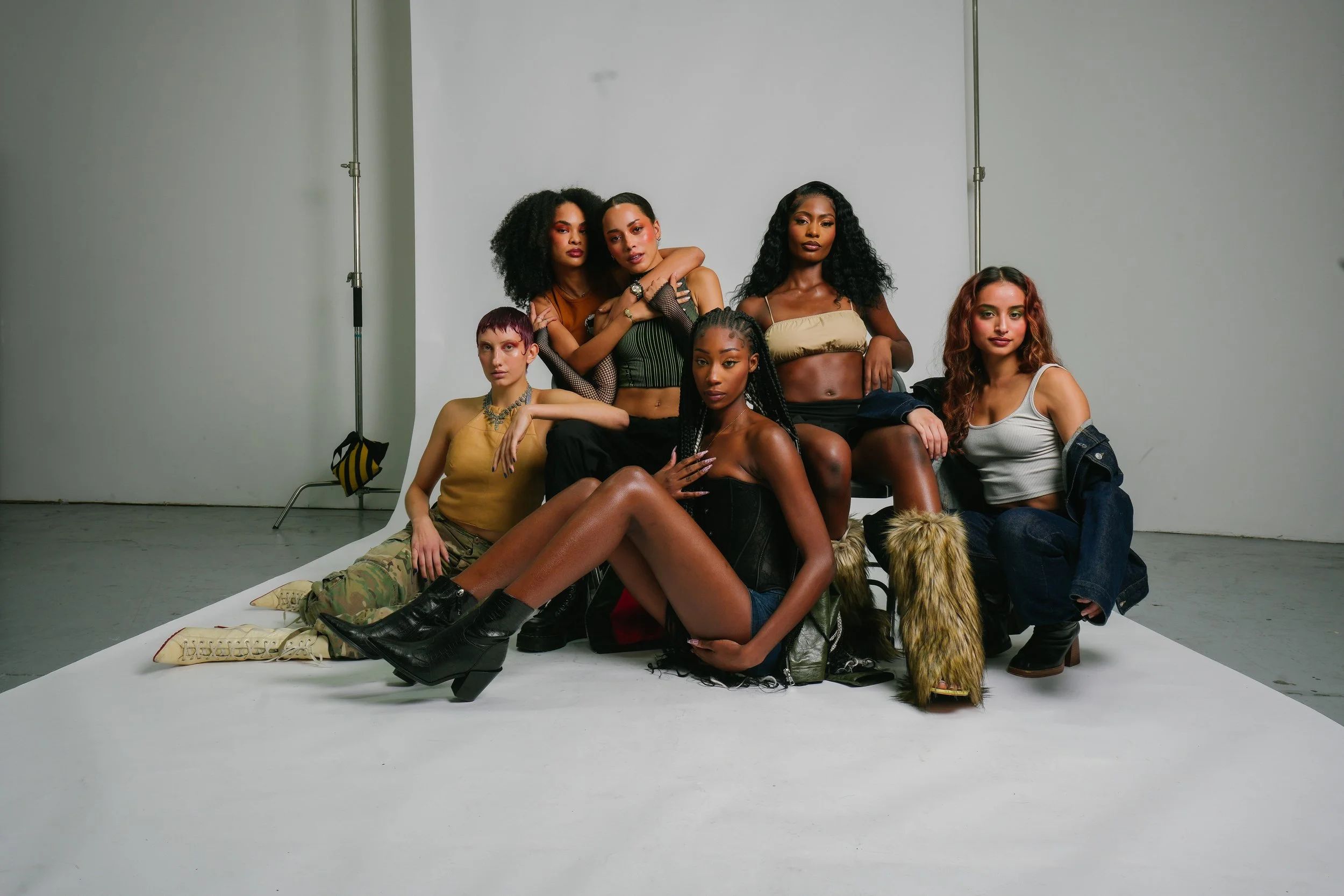 Group of six diverse women posing together in a photo studio with a white background, sitting and standing on a white floor.