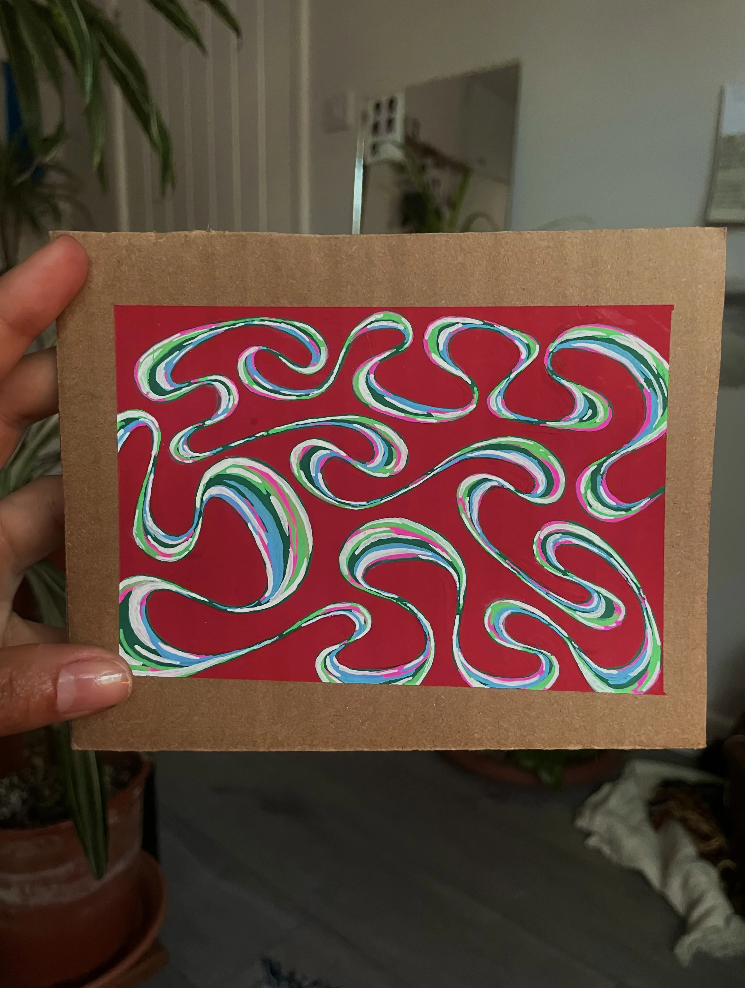 Close-up of a hand holding a cardboard frame with an abstract, colorful swirling pattern on red paper inside.