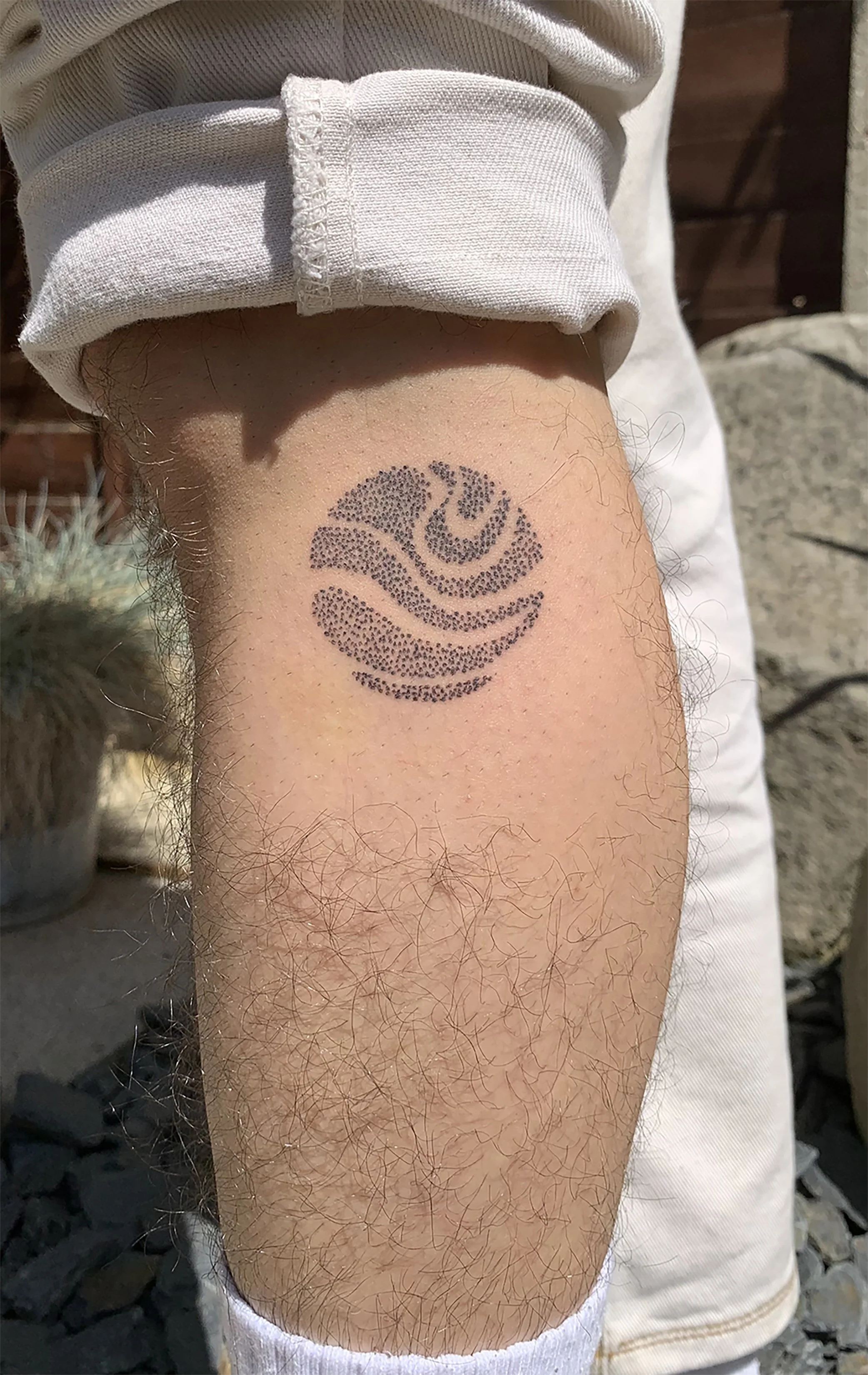 A person's forearm with a tattoo of a stylized leaf design in black ink.