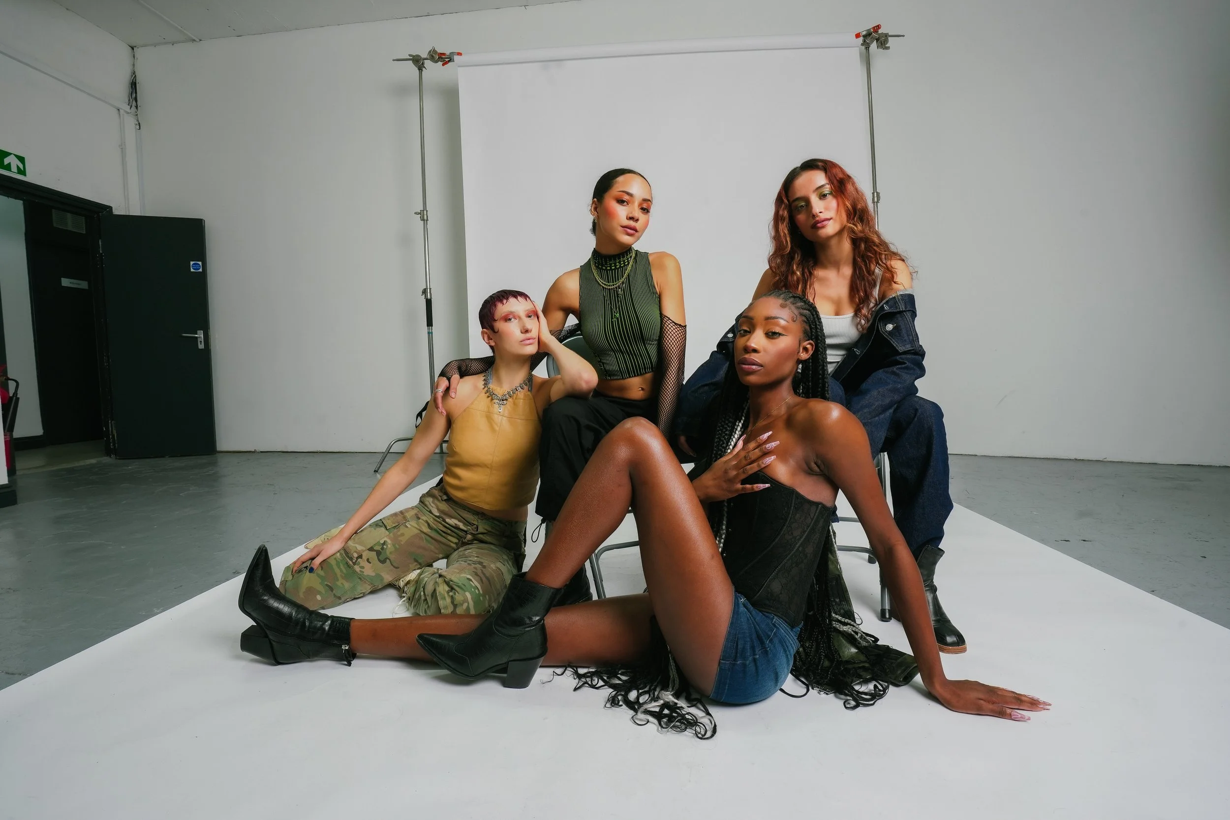 Group of five diverse young women posing in a photo studio with a white backdrop, dressed in stylish casual clothing and accessories.