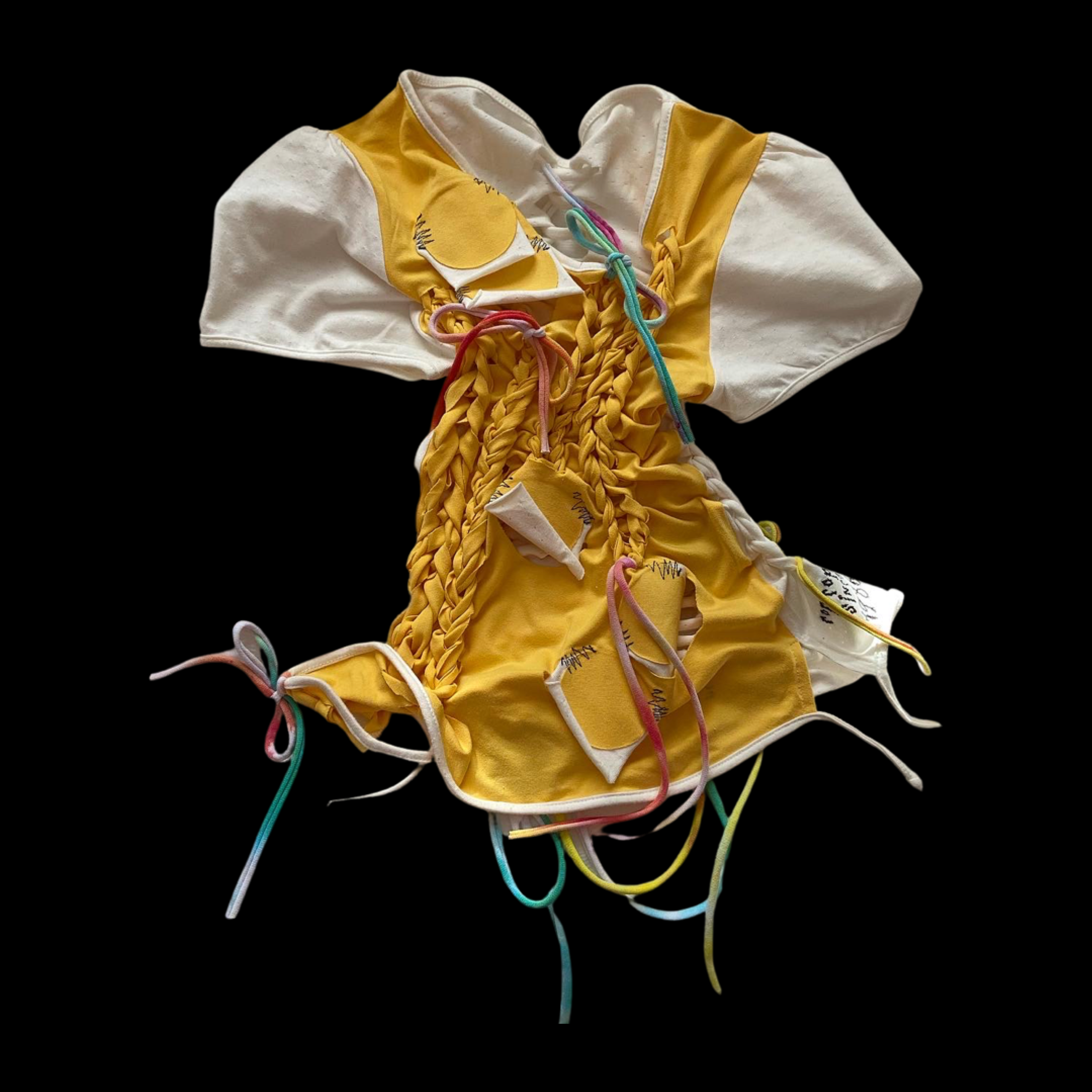 A yellow and white fabric garment with multicolored strings and woven details, placed on a black background.