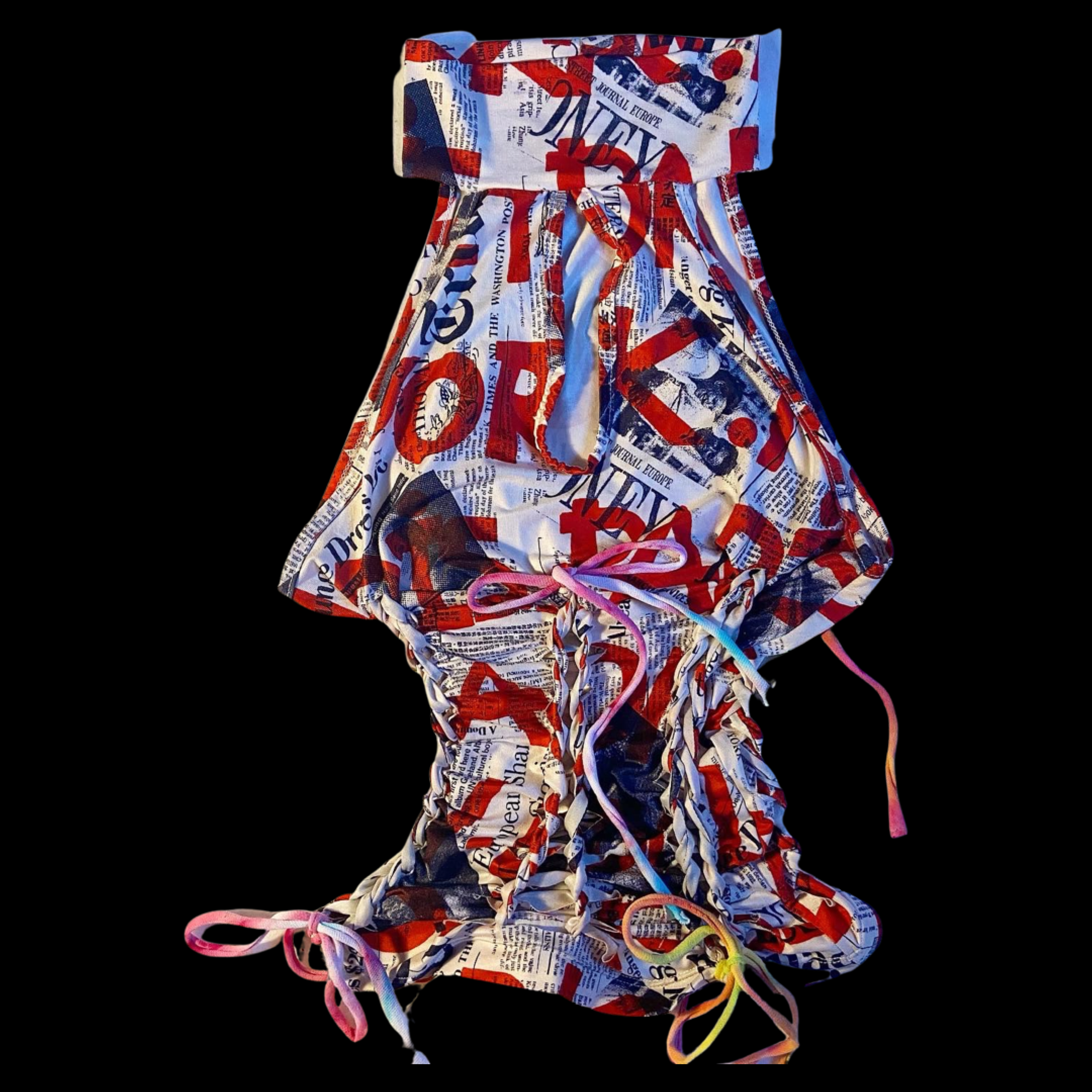 A fabric bag with a newspaper print pattern, tied with pink, white, and yellow laces at the top and the bottom on a black background.